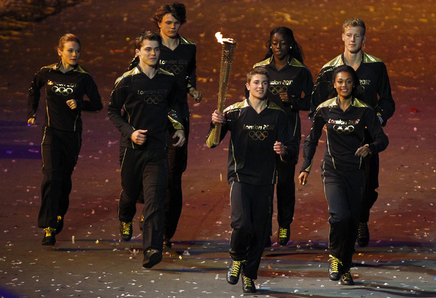 The Olympic torch is carried by seven young athletes towards the cauldron. 