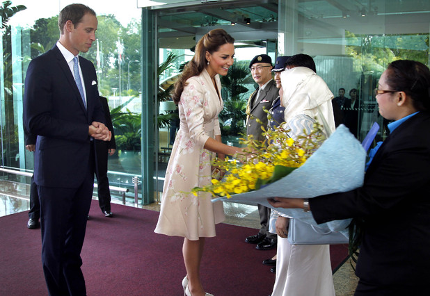 Prince William, the Duke of Cambridge, left, watches his wife Kate, the Duchess of Cambridge, center, receives flowers upon arrival at the VIP terminal of Changi International Airport on Tuesday, Sept. 11, 2012 in Singapore. The British royal couple is on an official three-day trip to Singapore. (AP Photo/Wong Maye-E, Pool)