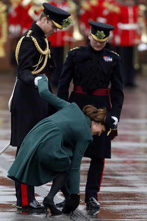 Kate Duchess of Cambridge bends down to pull the heel of her shoe out of a drainage grill after it got stuck.