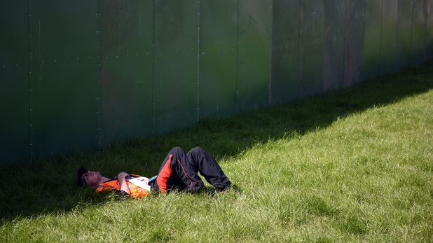 A steward rests in the shade of the perimeter fence at Glastonbury Festival 2015
